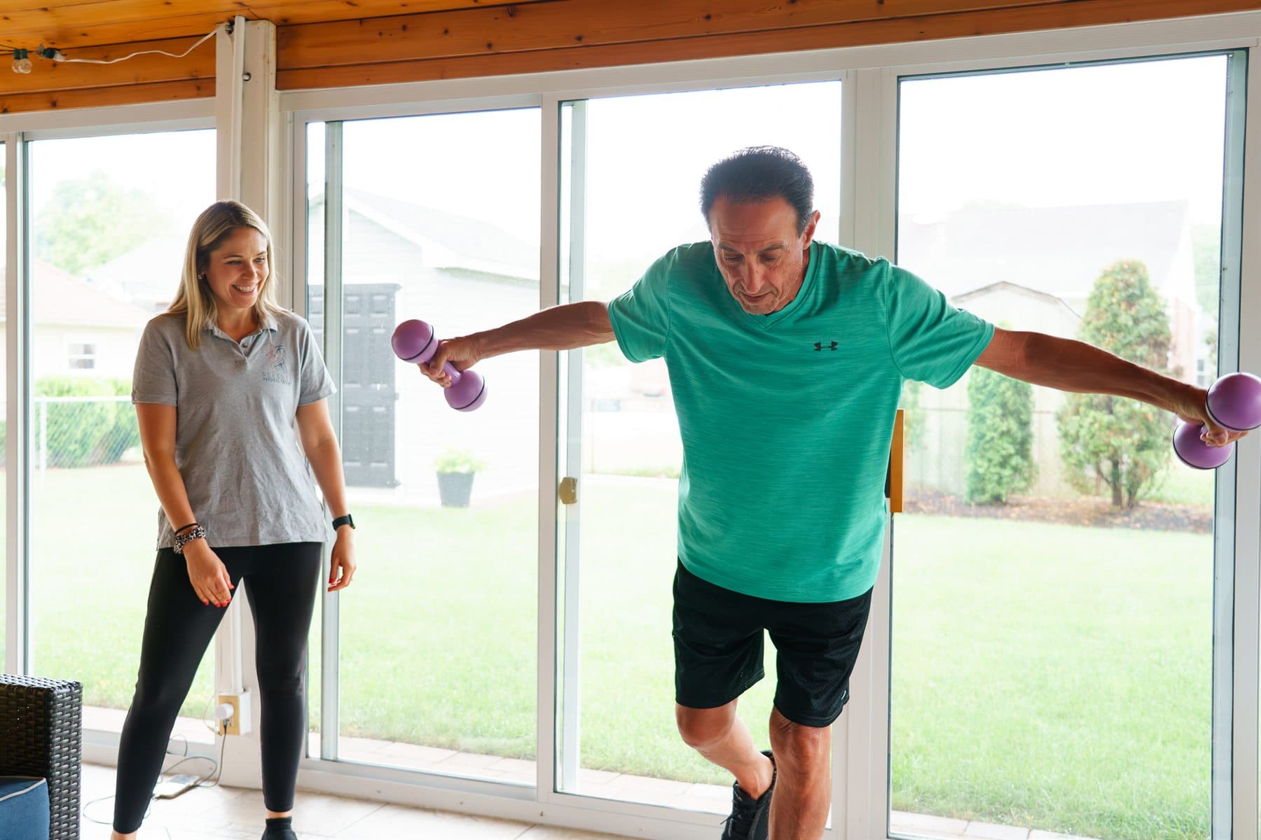 Nicole coaching an older adult through a standing balance exercise at home.